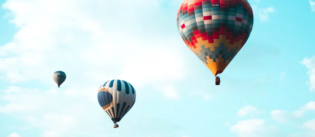 Warum Affiliate-Marketing? Bild: Drei Heißluftballons fliegen vor einem hellblauen Himmel mit Wolken.